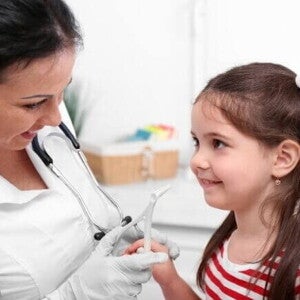 Menina com a boca aberta sendo examinada por um médico, simulando a avaliação de problemas respiratórios e de garganta relacionados à adenoide.