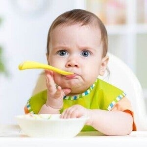 criança sentada em uma cadeira de alimentação com expressão curiosa enquanto come.