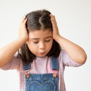 Menina de cabelo castanho com as mãos na cabeça, em uma expressão de desconforto ou dor. A imagem ilustra o sintoma, destacando a necessidade de saber como aliviar dor de cabeça em criança. Menina de cabelo castanho com as mãos na cabeça, em uma expressão de desconforto ou dor. A imagem ilustra o sintoma, destacando a necessidade de saber como aliviar dor de cabeça em criança.