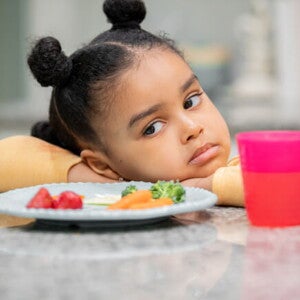 menina com semblante desconfiado olha para prato de comida sem vontade menina com semblante desconfiado olha para prato de comida sem vontade