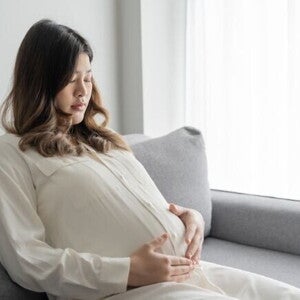 Mulher grávida pensativa sentada no sofá com as mãos na barriga. Mulher grávida pensativa sentada no sofá com as mãos na barriga.