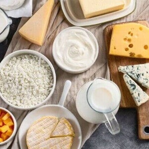 Visão aérea de uma mesa repleta de produtos lácteos variados. Os alimentos estão dispostos sobre um pano bege.