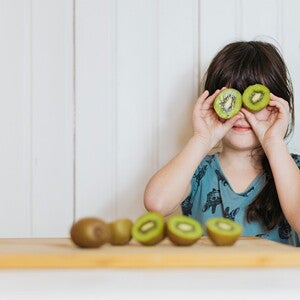 Deficiências nutricionais e Estudo Nacional de Alimentação e Nutrição Infantil (ENANI) menina segurando duas rodelas de kiwi