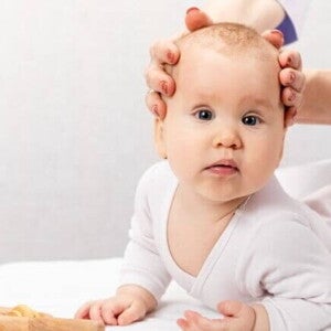 Um bebê deitado com a sua cabeça sendo segurada por duas mãos Um bebê deitado com a sua cabeça sendo segurada por duas mãos