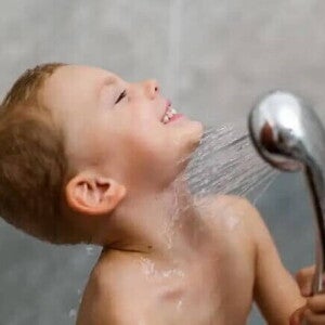 Um menino toma banho sozinho, exercitando sua autonomia infantil, com a ajuda de uma ducha móvel. 