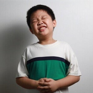 Criança com expressão de dor abdominal ou desconforto, segurando a barriga, representando sintoma de barriga de lombriga.