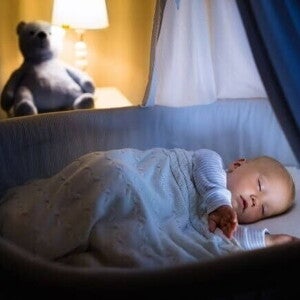 Bebê dormindo calmamente no berço à noite, sob uma luz amarela suave, representando um bebê que dorme bem.