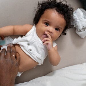 bebê de fralda e body branco, com a mão de adulto sobre a barriga bebê de fralda e body branco, com a mão de adulto sobre a barriga