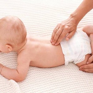 bebê deitado de bruços e uma mão segundo sua perna e outra massageando sua lombar bebê deitado de bruços e uma mão segundo sua perna e outra massageando sua lombar