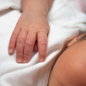 bebê recém nascido, com substância esbranquiçada em uma das mãos