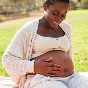 Mulher grávida sorrindo sentada na grama e acariciando a barriga Mulher grávida sorrindo sentada na grama e acariciando a barriga