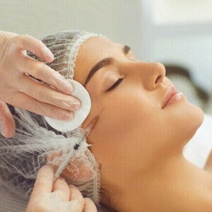 Close-up de uma mulher recebendo uma injeção de Botox ou preenchimento facial em uma clínica de estética, com a profissional usando luvas e uma seringa, representando o procedimento estético.