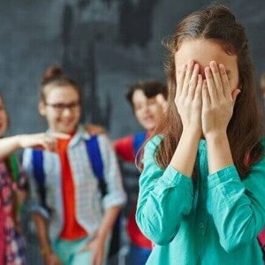 Grupo de crianças apontando e rindo de uma menina que está cobrindo o rosto com as mãos Grupo de crianças apontando e rindo de uma menina que está cobrindo o rosto com as mãos