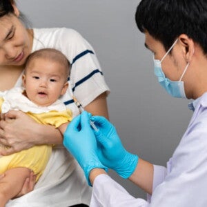 imagem de um bebê no colo de uma mulher adulta e um homem segurando uma seringa, vestindo roupas de profissionais da saúde na cor branca imagem de um bebê no colo de uma mulher adulta e um homem segurando uma seringa, vestindo roupas de profissionais da saúde na cor branca