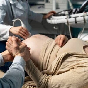 Uma gestante deitada em um consultório médico, segurando a mão de um homem, durante um exame de ultrassom Uma gestante deitada em um consultório médico, segurando a mão de um homem, durante um exame de ultrassom