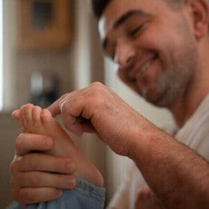 Um homem sorrindo e segurando o pé de uma criança fazendo um movimento de cócegas com o dedo. Um homem sorrindo e segurando o pé de uma criança fazendo um movimento de cócegas com o dedo.