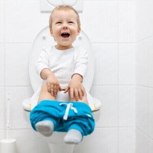 Criança pequena feliz sentada no vaso sanitário, celebrando o sucesso do desfralde.