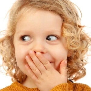 Criança pequena com expressão de vergonha ou timidez, cobrindo a boca.