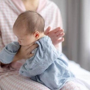 Posição clássica de como fazer para bebe arrotar: a mãe segura o bebê confortavelmente contra o ombro com um pano de boca para protegê-la contra golfadas de leite ou saliva.