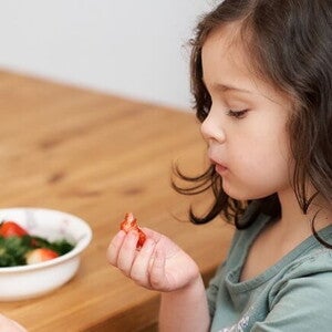 Criança pegando um alimento que está no prato na sua frente Criança pegando um alimento que está no prato na sua frente
