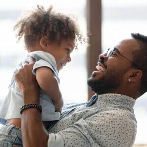 Uma criança é carregada pelo seu pai. Os dois estão brincando e sorrindo. A imagem remete ao tema crise dos três anos Uma criança é carregada pelo seu pai. Os dois estão brincando e sorrindo. A imagem remete ao tema crise dos três anos
