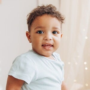 Criança vestindo blusa azul claro em um quarto de cores neutras e luzes de decoração Criança vestindo blusa azul claro em um quarto de cores neutras e luzes de decoração