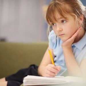 Uma menina com olhar concentrado, apoia a cabeça sobre a mão, enquanto segura um lápis sobre o caderno Uma menina com olhar concentrado, apoia a cabeça sobre a mão, enquanto segura um lápis sobre o caderno