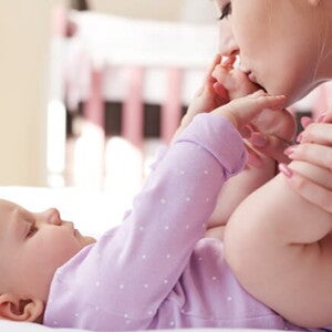 Mãe embalando carinhosamente as perninhas do seu bebê que está deitado na cama Mãe embalando carinhosamente as perninhas do seu bebê que está deitado na cama