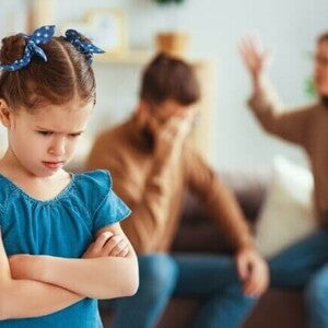 Criança emburrada com pais discutindo ao fundo, representando o impacto do divórcio nos filhos.