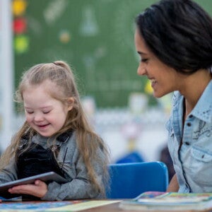 Criança com Síndrome de Down segurando um tablet ao lado da professora na escola Criança com Síndrome de Down segurando um tablet ao lado da professora na escola