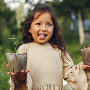 menina sorri e mostra a língua enquanto segura dois vasos de plantas menina sorri e mostra a língua enquanto segura dois vasos de plantas