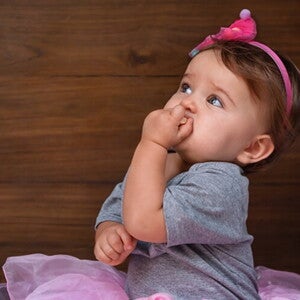 Menina de aproximadamente um ano usando vestido rosa e com a mão na boca. Menina de aproximadamente um ano usando vestido rosa e com a mão na boca.