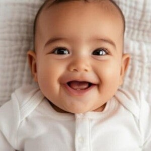 Bebê usando roupa branca em cima de um edredom sorrindo Bebê usando roupa branca em cima de um edredom sorrindo