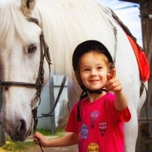 Menina sorrindo e apontando com o dedo, enquanto segura a rédea de um cavalo Menina sorrindo e apontando com o dedo, enquanto segura a rédea de um cavalo