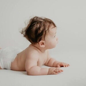 Um bebê deitado de bruços, com uma expressão de surpresa, olhando para o lado. A imagem pode ser usada para ilustrar o desenvolvimento e a saúde infantil, incluindo condições como a espinha bífida.