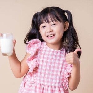Menina sorrindo, vestindo um vestido xadrez rosa e branco, segurando um copo de leite e fazendo um joinha Menina sorrindo, vestindo um vestido xadrez rosa e branco, segurando um copo de leite e fazendo um joinha
