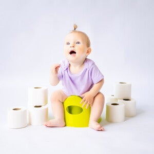 Foto de bebê sentada no penico rodeado por rolos de papel higiênico