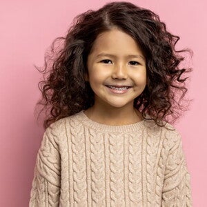 Menina de cabelo ondulado sorrindo em frente a uma parede cor de rosa. Menina de cabelo ondulado sorrindo em frente a uma parede cor de rosa.
