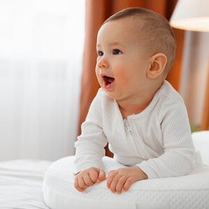 Bebê usando macacão branco deitado de barriga para baixo em cima da cama. Bebê usando macacão branco deitado de barriga para baixo em cima da cama.