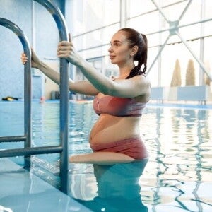 Mulher grávida praticando exercícios leves dentro de uma piscina Mulher grávida praticando exercícios leves dentro de uma piscina