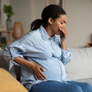 Mulher grávida sentada em um sofá, com uma mão na barriga e a outra mão na boca. Mulher grávida sentada em um sofá, com uma mão na barriga e a outra mão na boca.
