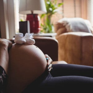 imagem com foco na barriga de uma mulher grávida, com dois sapatinhos de bebê na cor branca posicionados acima da barriga imagem com foco na barriga de uma mulher grávida, com dois sapatinhos de bebê na cor branca posicionados acima da barriga