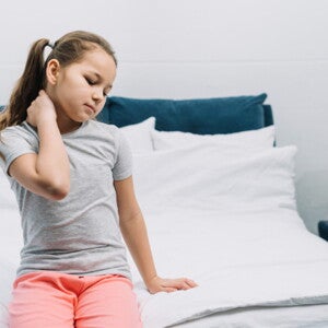 imagem de uma menina sentada na beira de uma cama, com uma das mãos no pescoço e com olhos fechados imagem de uma menina sentada na beira de uma cama, com uma das mãos no pescoço e com olhos fechados