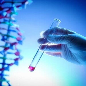 Mão com luva de laboratório segurando um tubo de ensaio com líquido avermelhado, em frente a uma representação em 3D da dupla hélice do DNA, em um ambiente de luz azulada.