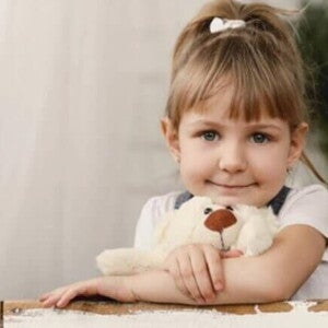 Menina de aproximadamente 4 anos apoiada na mesa abraçada com seu ursinho de pelúcia Menina de aproximadamente 4 anos apoiada na mesa abraçada com seu ursinho de pelúcia