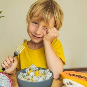Um menino sentado à mesa com um prato de frutas variadas segurando um garfo e piscando um olho. A imagem representa um lanche da tarde para crianças com frutas saudáveis. Um menino sentado à mesa com um prato de frutas variadas segurando um garfo e piscando um olho. A imagem representa um lanche da tarde para crianças com frutas saudáveis.