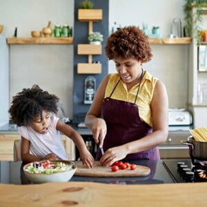 mulher pica legumes sob mesa de cozinha com criança ao lado interagindo mulher pica legumes sob mesa de cozinha com criança ao lado interagindo