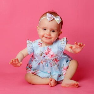 Bebê usando vestido florido e laço na cabeça em um ambiente com fundo cor de rosa. Bebê usando vestido florido e laço na cabeça em um ambiente com fundo cor de rosa.