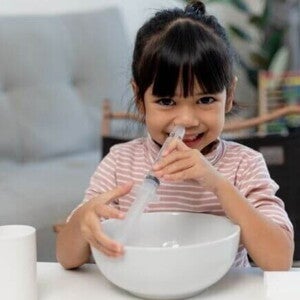 Um bebê deitado com a boca aberta, enquanto uma mão segura uma seringa próxima ao nariz do bebê Um bebê deitado com a boca aberta, enquanto uma mão segura uma seringa próxima ao nariz do bebê