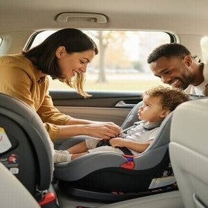 Pais assegurando a cadeirinha de um filho pequeno no carro, focando na segurança infantil.